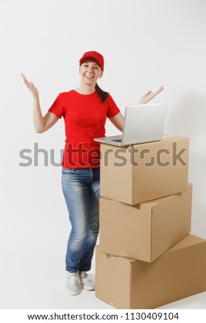 Full length portrait of delivery woman in red cap, t-shirt isolated on white background. Female courier standing near empty cardboard boxes with laptop pc computer. Receiving package. Copy space