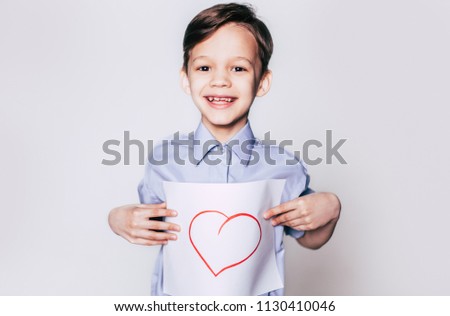 Love sign, heart picture on paper. Smiling handsome teen brunette boy in casual wear posing on gray background