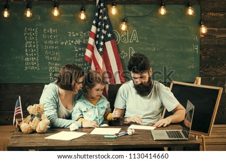 Home school. Kid with parents in classroom with usa flag, chalkboard on background. American family sit at desk with son and usa flag. Parents teaching son american traditions playing.