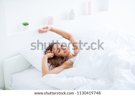 Portrait of attractive lovely girl enjoying time in bad after sleeping lying under blanket making stretching keeping eyes closed. Good day life health concept Royalty-Free Stock Photo #1130419748