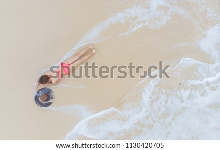 Top view Young woman in a pink bikini lying and relaxing on the white sandy beach with turquoise sea water of thailand,aerial view from drone / Summer concept.