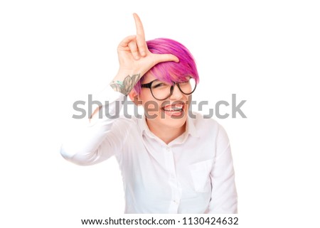 Cheerful young woman with pink short hair showing loser sign and laughing with mockery at camera isolated on white background