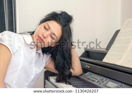 Attractive woman sitting near piano. Pretty woman sitting near a synthesizer and dreaming