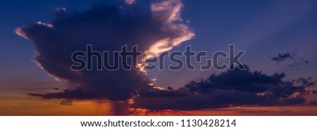 Beautiful sky at sunset with a huge cloud in dark orange and dark blue colors. Heavenly dramatic background