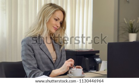 Beautiful businesswoman in suit works with cup coffee at workplace