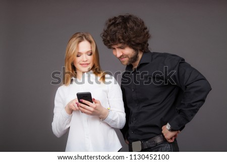 young blond woman and brunette man looking in one smartphone. Photo taken in studio on a gray background