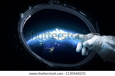 Astronaut click on power button on hud display in the porthole. Earth on the background. Elements of this image furnished by NASA
