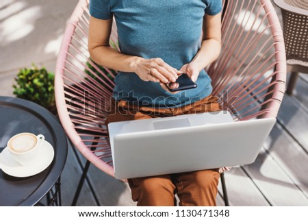 Young woman using laptop and smartphone in a city. Beautiful girl sitting in a cafe and working on computer