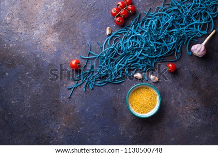 Blue Colored Pasta with Cherry Tomatoes, Garlic and Lemon Salt on Dark Background. Flat Lay. Copy space. Top view.