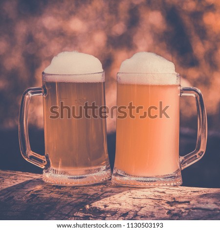 two beer with foam in mug on green outdoor background, vintage toning picture