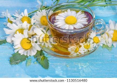 A cup of tea with chamomile, close-up, lit by sunlight, on a light blue wooden table.