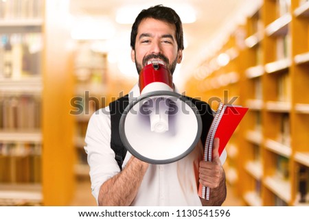 Student man shouting by megaphone on defocused library