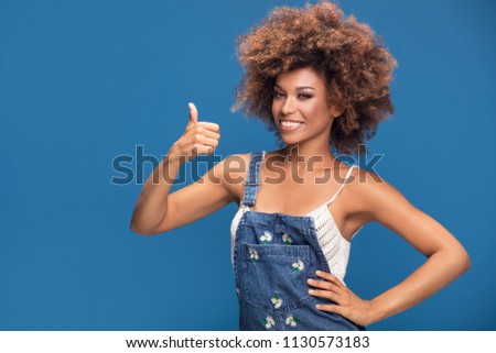 Smiling beautiful young African American woman with curly afro hair smiling to the camera, showing okay symbol.