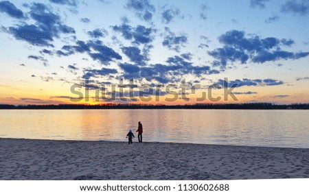 Silhouettes of people on the beach with background of mirror-smooth river during sunset under a beautiful cloudy sky