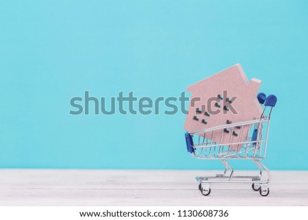 Model of the wooden house in shopping cart on wooden table with blue background