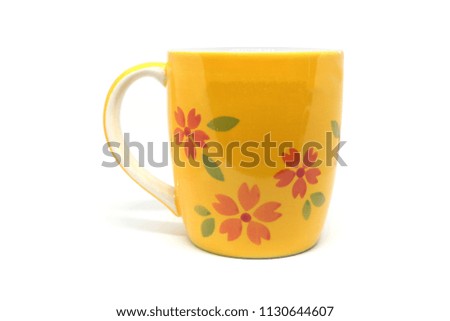 Yellow mug with red flowers and green leaves isolated on white background.