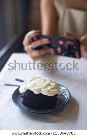 woman taking picture of dark chocolate cake with cream cheese on the table.