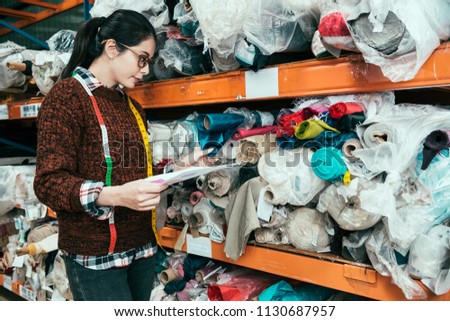 Asian woman manager searching the appropriate texture for the client. She is touching the fabric in the warehouse.