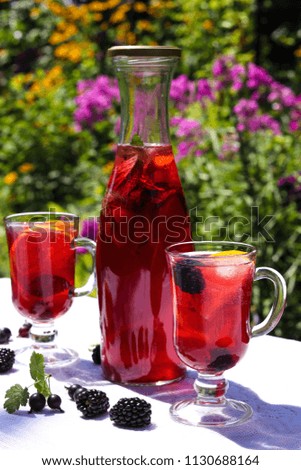 Home-made fruit lemonade is in a bottle and glasses on a table in the open air against a background of flowers. Healthy eating.