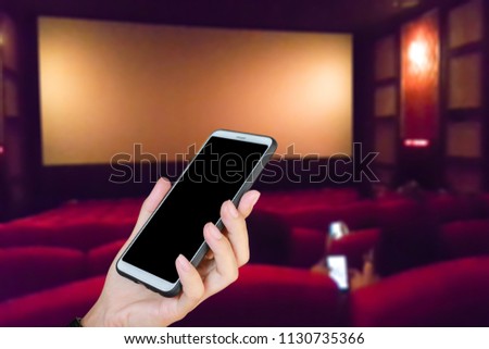 Man use mobile phone, blur image of inside the movie theater as background.