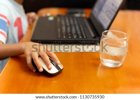 Selected focus childrens hand using laptop computer mouse with glass of water