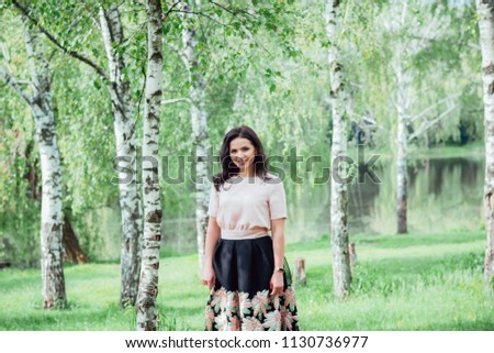 Dreamy young lady relaxing in the meadow during recreation time in sunny day, beautiful woman enjoying spring nature while walking in park. Girl wearing in pink satin blouse and black bell-skirt