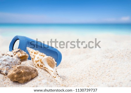 Portable wireless speaker and Sea shells on sand. Blue sky Summer beach background.