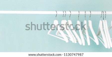 Many wooden white hangers on a rod, isolated on blue turquoise wall background. Store concept, sale, design, empty hanger. Place for text.