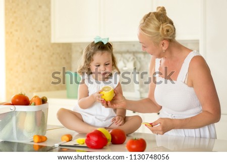 Mom shows a lemon to a girl in a white kitchen