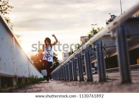 Happy skater girl walking through city holding long-board in the sunset