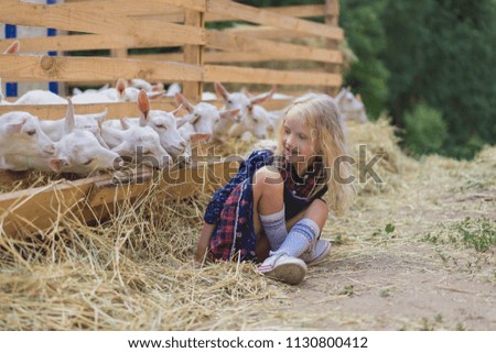 child sitting on hay near goats behind fences at farm