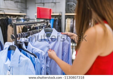 Happy Woman In Retail Clothing Shop. Shopper Looking At Price Tag. Beautiful woman shopping trendy clothes. Shopaholic woman shopping clothes on sale. Buying clothes 
