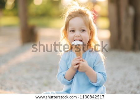 Beautiful little girl in a blue dress eating an ice cream