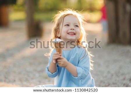 Beautiful little girl in a blue dress eating an ice cream Royalty-Free Stock Photo #1130842520
