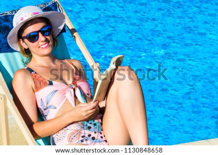 Beautiful girl reading a book in the pool totally relaxed with a shining sun.