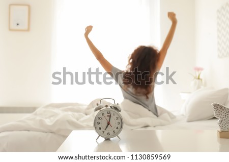 Alarm clock on table in bedroom of beautiful young woman. Morning time Royalty-Free Stock Photo #1130859569