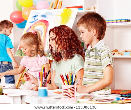 Children with teacher painting at easel in school.