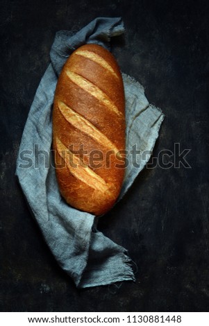 Fresh homemade bread on a cutting board on a dark background. French bread.  Fresh crispy white bread. Loaf of bread. Dark photo.