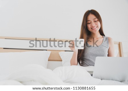 Asian beautiful smiling women using laptop and drink coffee on white bed in bedroom interior morning.Concept of people lifestyle use technology.