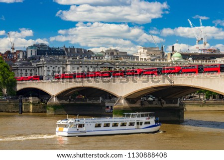 Red buses queue on Waterloo Bridge transporting commuters while a boat ferries tourists along the river 