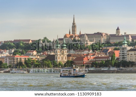 Budapest cityscape. Beautiful architecture with the Fisherman's Bastion on the Buda hill towering over the river under the blue sky in warm light of the setting sun. Ships sailing on the Danube.