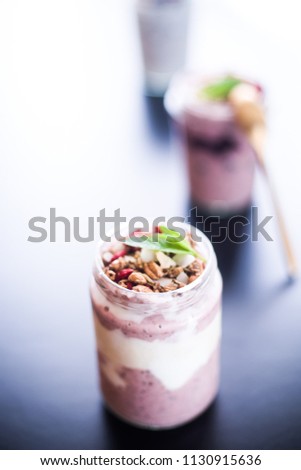Vanilla and strawberries chia parfait on a glass mason jarr topped with blueberres, shallow depth of field, selective focus technique, strong backlight over a reflective  daark board