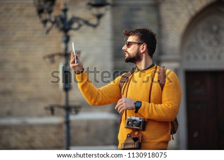 Portrait of a young man holding a mobile phone while sightseeing in a foreign city