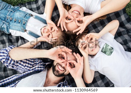 Funny picture of family doing funny rounds with their fingers on eyes. They are playing. All of them are lying on blanket and smiling. They look happy.