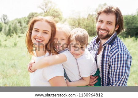 Portrait of a beautiful family standing together. Woman is golding her daughter on the back while man is holding his son in front on him on hands.