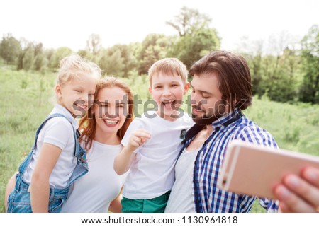 Gorgeous family is taking selfie. Guy is holding phone and looking down. Everybody else is looking on phone and smiling.