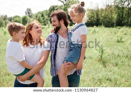 A picture o friendly family. Man and woamn are holding kids on their hands. They are looking at each other with unconditional love. They all are very happy.