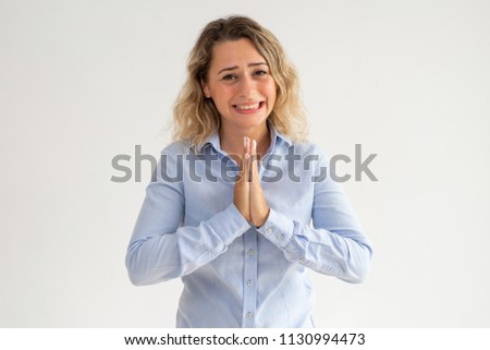 Scared young woman holding hands together and begging. Upset curly-haired female employee praying and asking about forgiveness. Despair concept Royalty-Free Stock Photo #1130994473