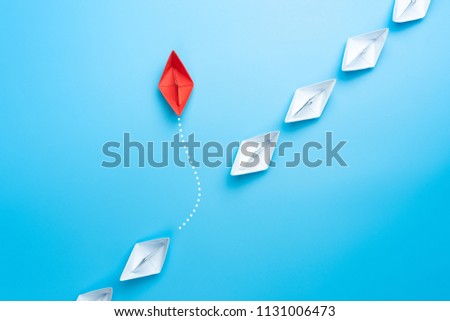 Group of white paper ship in one direction and one red paper ship pointing in different way on blue background. New idea, Unique way and Business for innovative solution concept.