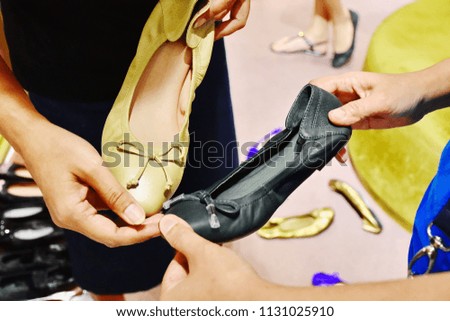 Unrecognizable woman with friend shopping ballet shoes in shop, two hand holding black and beige beautiful design fashion leather shoe with blurred gold shoes and  other customer at department store 